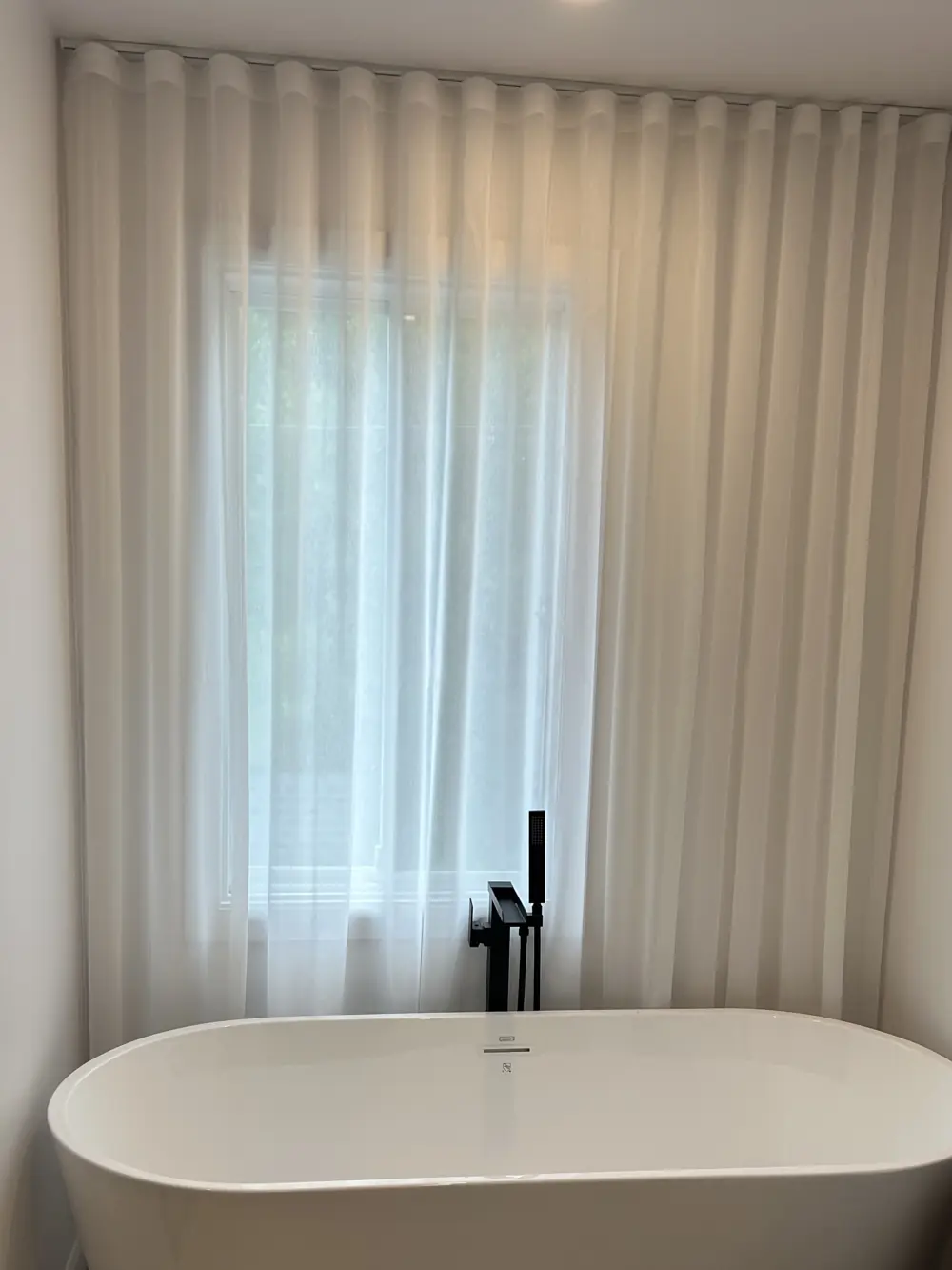 Salle de bain avec voilage ripplefold blanc derrière un bain autoportant